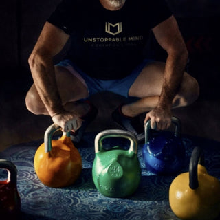 Load image into Gallery viewer, Man squatting with colorful kettlebells on a dark surface