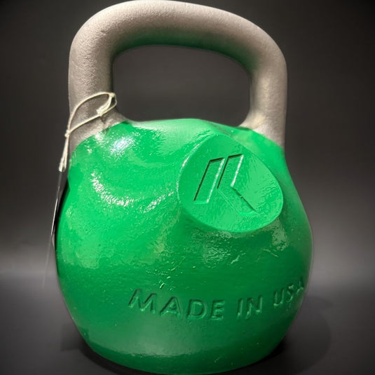 A green cast iron kettlebell with a gray handle, featuring an embossed logo and 'MADE IN USA' text on the front, set against a dark gray background.