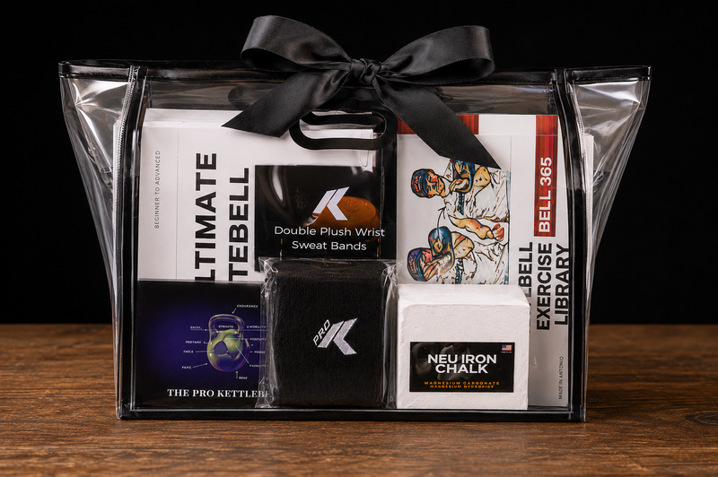 Load image into Gallery viewer, A black gift basket with a black ribbon bow, containing a curated fitness and kettlebell equipment bundle. The bundle includes Ultimate Tebell kettlebell books, a Double Plush Wrist Sweat Band, a black wristband with a white 'K' logo, a Neu Iron Chalk book, and a Bell 365 Exercise Library book, all neatly arranged inside a clear plastic gift bag on a wooden surface against a black background.
