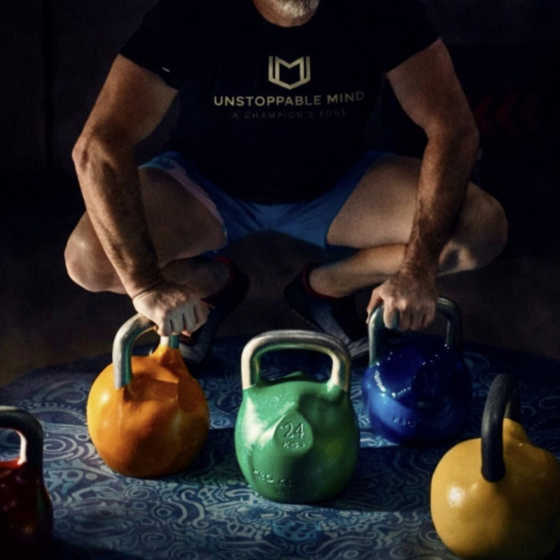 Load image into Gallery viewer, Man squatting with colorful kettlebells on a dark surface
